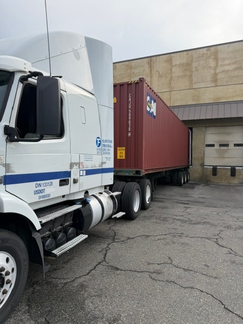 Flintstone Trucking semi-truck hauling a red container at a loading dock